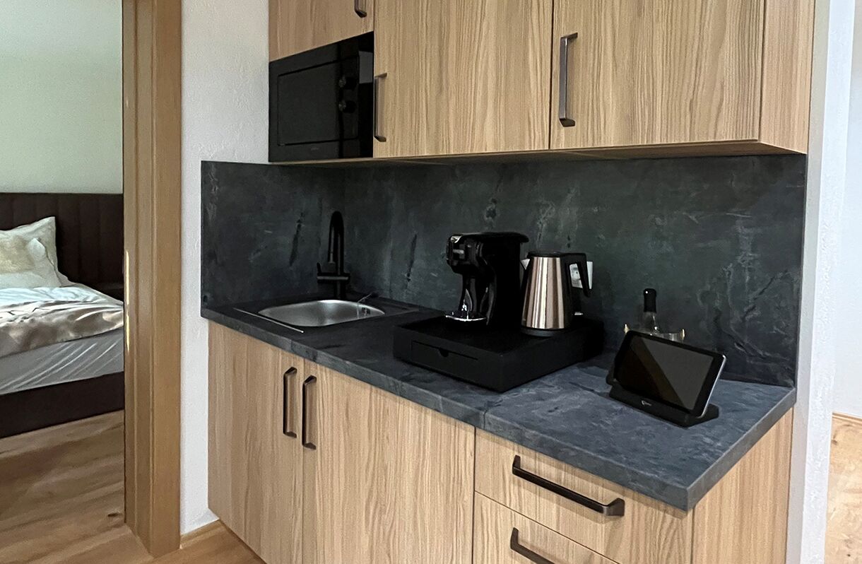 A compact kitchen with a sink, a coffee maker, and a tablet on the counter.