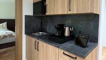 A compact kitchen with a sink, a coffee maker, and a tablet on the counter.