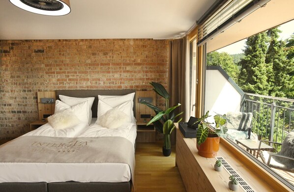 Un dormitorio con pared de ladrillo, cama con cubrecama blanco y balcón con plantas.