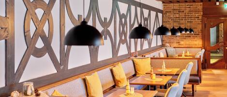 A restaurant with wooden benches and tables, pendant lighting, and a brick wall with a decorative pattern.