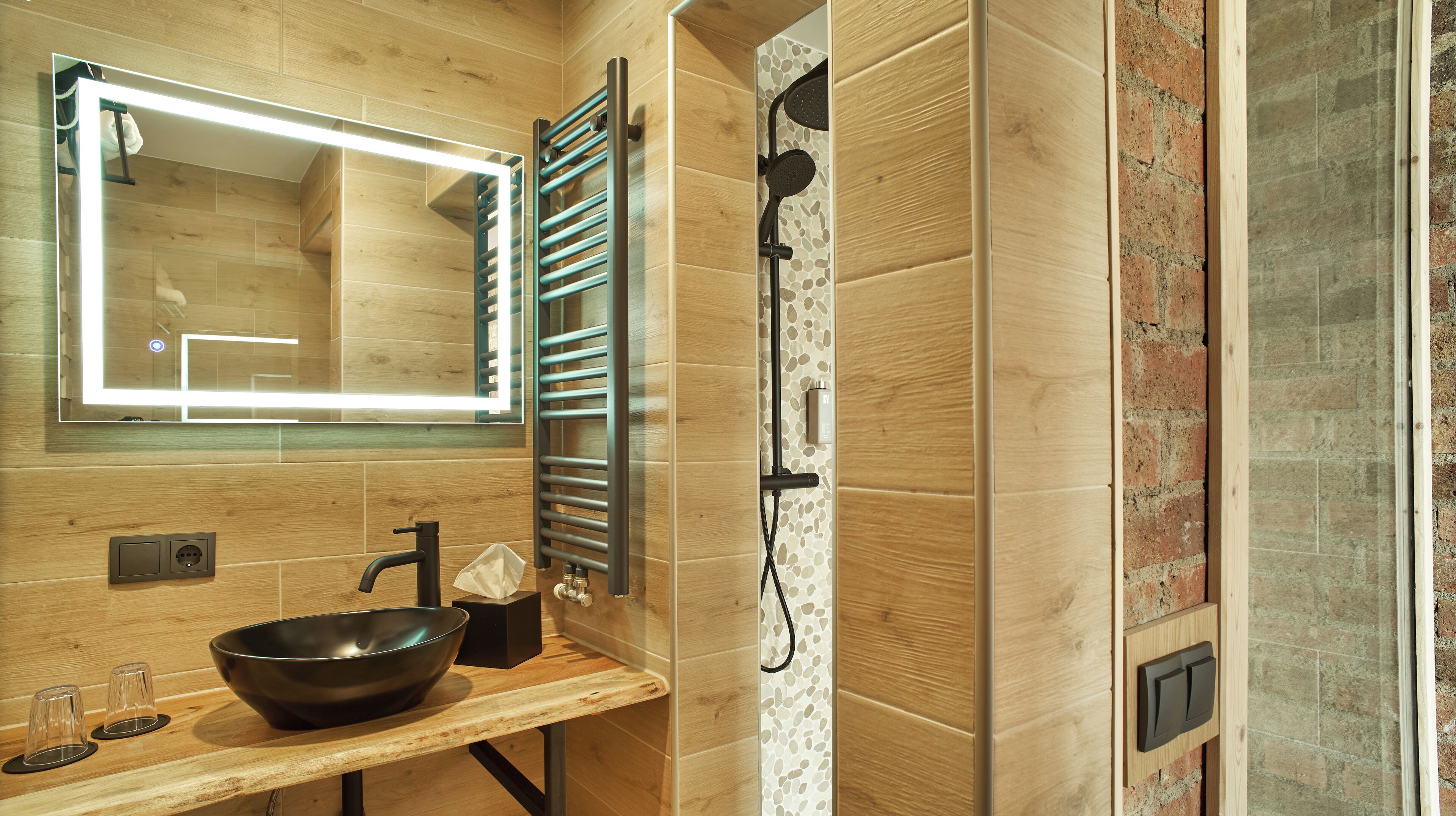 A modern bathroom with a wooden vanity, a large mirror, a towel rack, and a shower area.