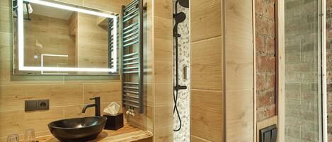 Un baño moderno con tocador de madera, un espejo grande, un perchero para toallas y una zona de ducha.