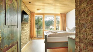 Un dormitorio con techo de madera, cama, ventana con cortinas y vistas a árboles.