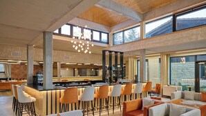 Un interior espacioso y moderno con una zona de bar, disposición de asientos y grandes ventanales que proporcionan luz natural.