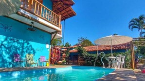 Un'area piscina con pavimento in legno, una zona relax coperta e un edificio con un balcone.