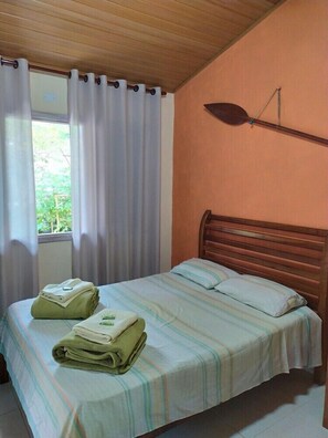 A bedroom with a wooden headboard, a bed with striped bedding, and a window with white curtains.