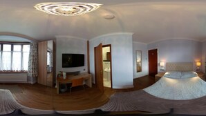 Et panoramaudblik over et hotelværelse med en bueseng, et skrivebord med et fladskærms-tv, et badeværelse med håndvask og spejl samt et stort vindue med gardiner.