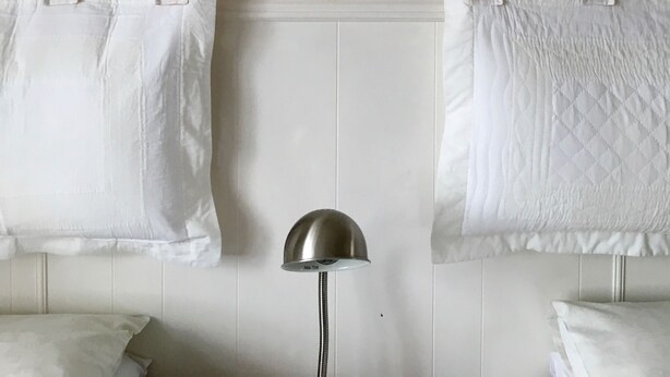 Et værelse med to hvide senge, et billede i ramme på væggen og en gulvlampe.