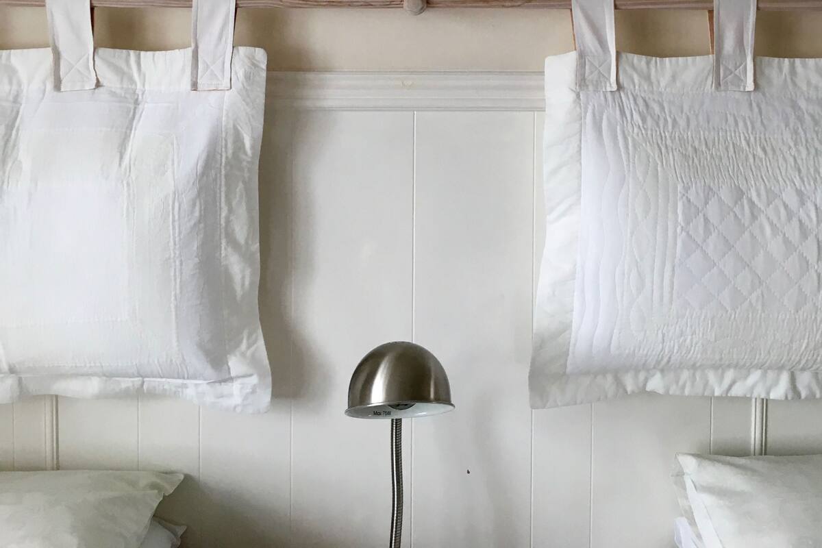 A room with two white beds, a framed picture on the wall, and a floor lamp.