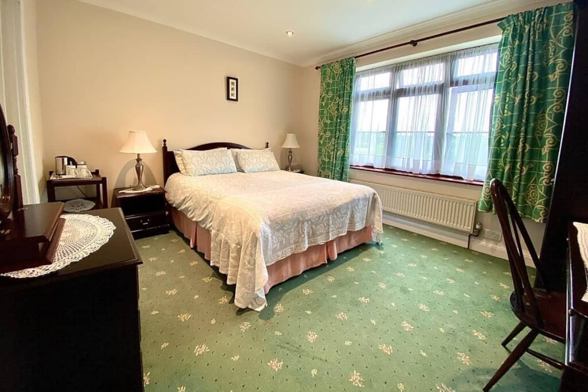 A bedroom with a bed, two bedside tables, a dresser, a chair, and a window with curtains.