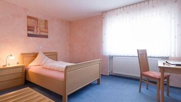 A bedroom with a bed, bedside table, chair, and a window with curtains.