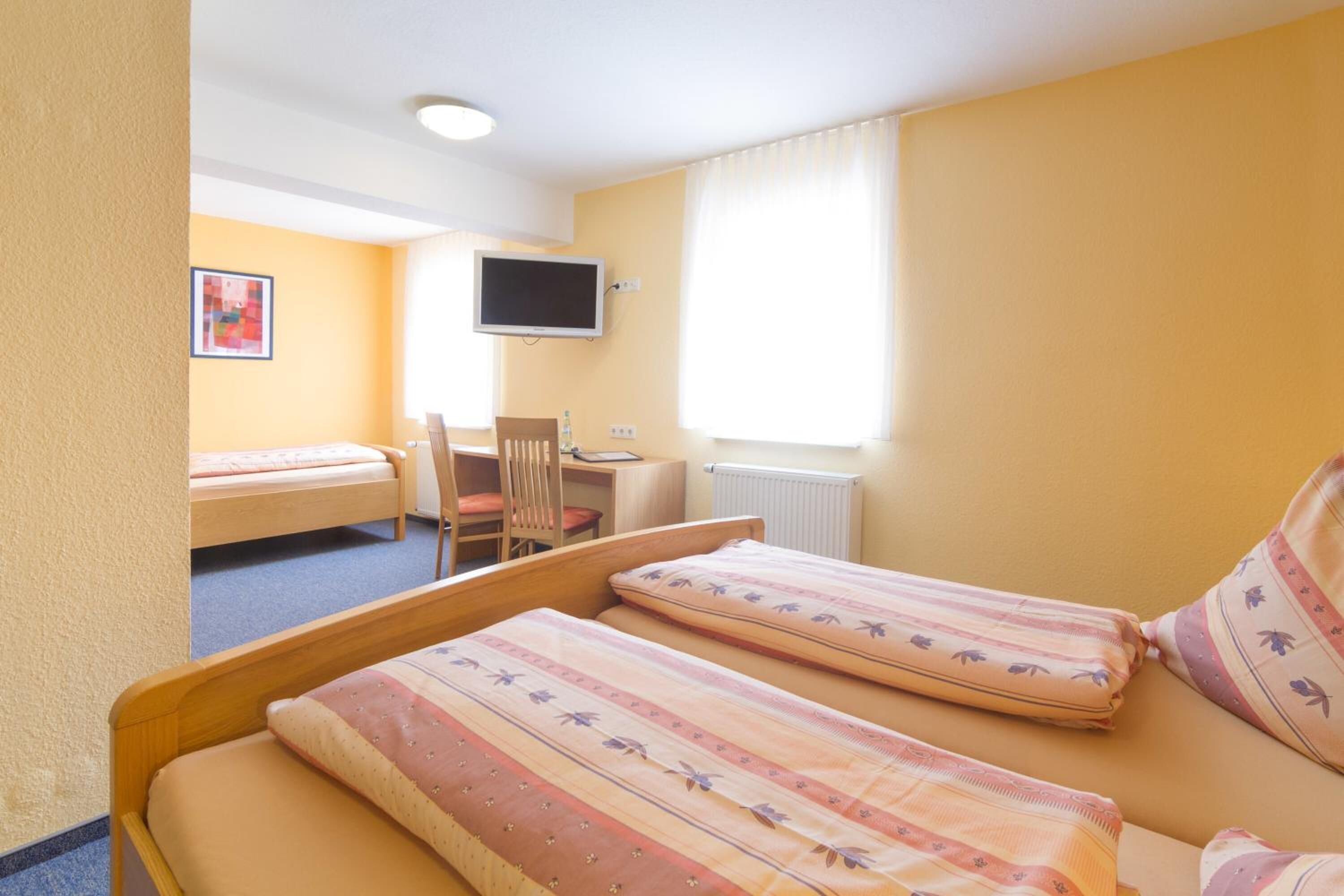 A hotel room with two single beds, a desk, a chair, a television, and a window with curtains.