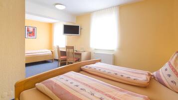 A hotel room with two single beds, a desk, a chair, a television, and a window with curtains.