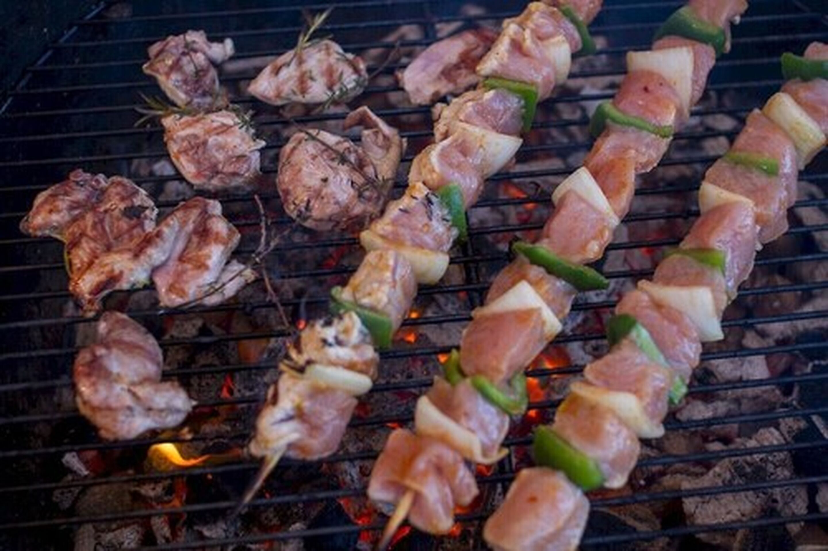 Brochetas de carne y verduras asándose sobre fuego abierto.