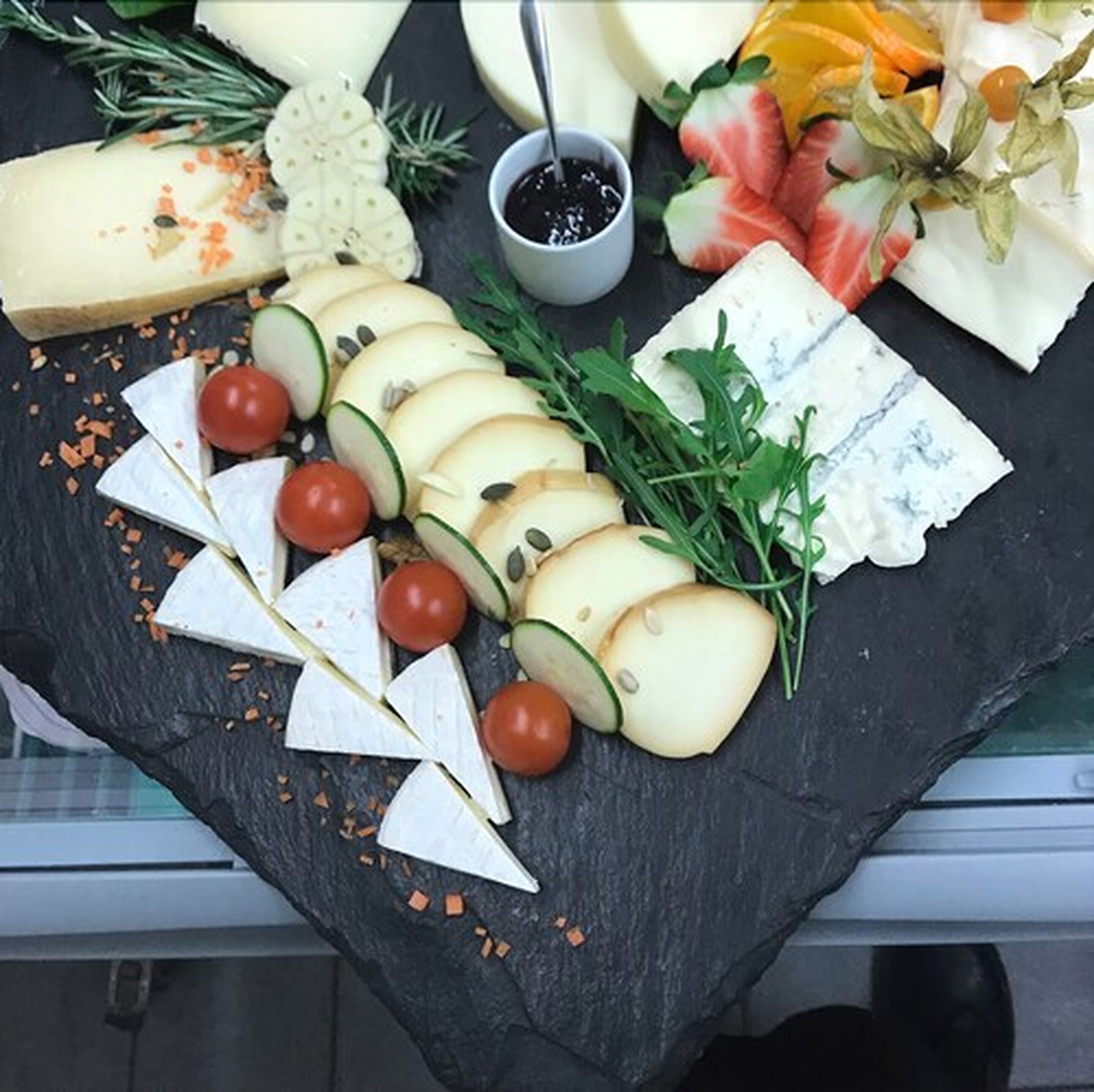 A cheese board with various cheeses, tomatoes, and herbs.