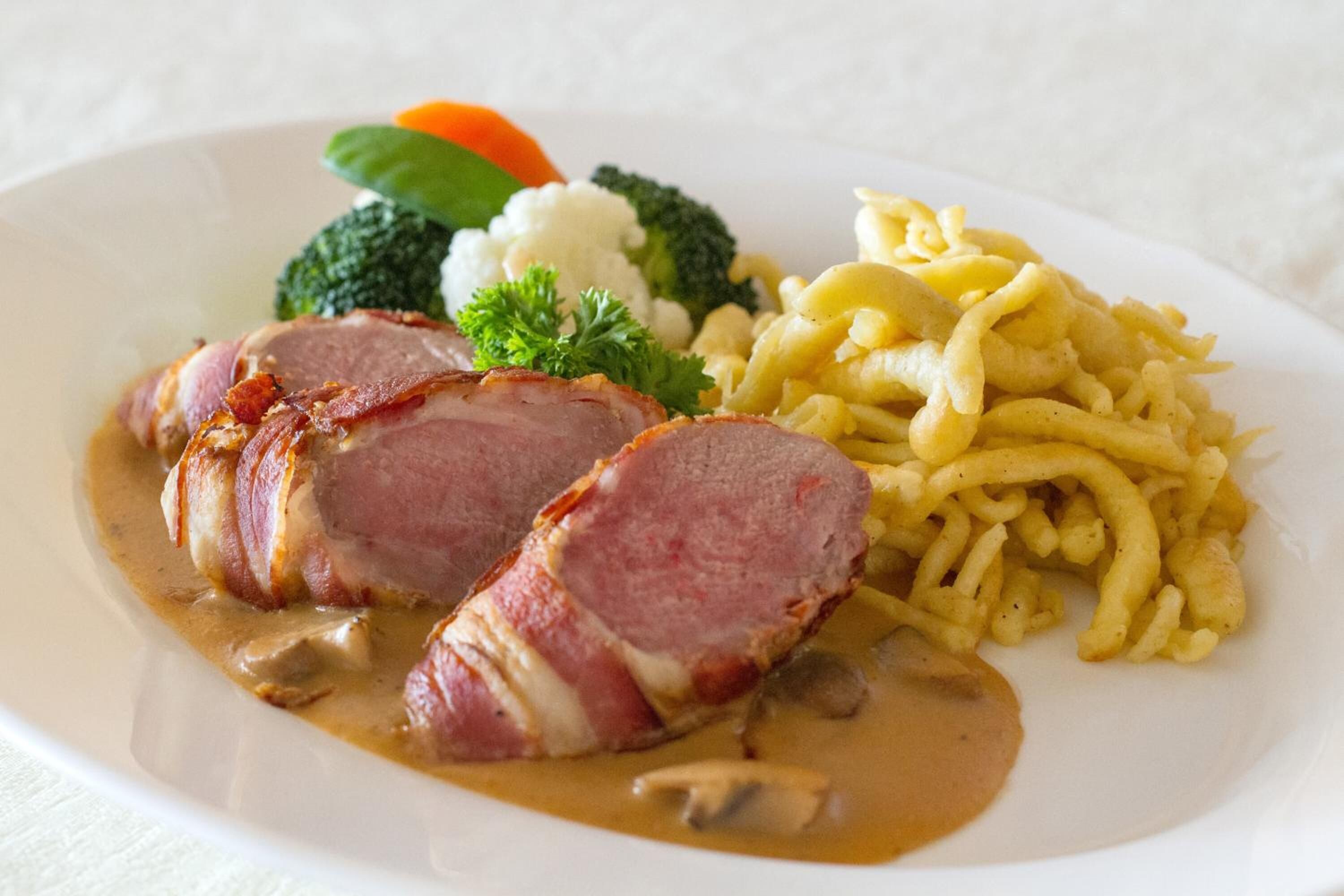 A plate with sliced ham, mushrooms, broccoli, carrots, and macaroni.
