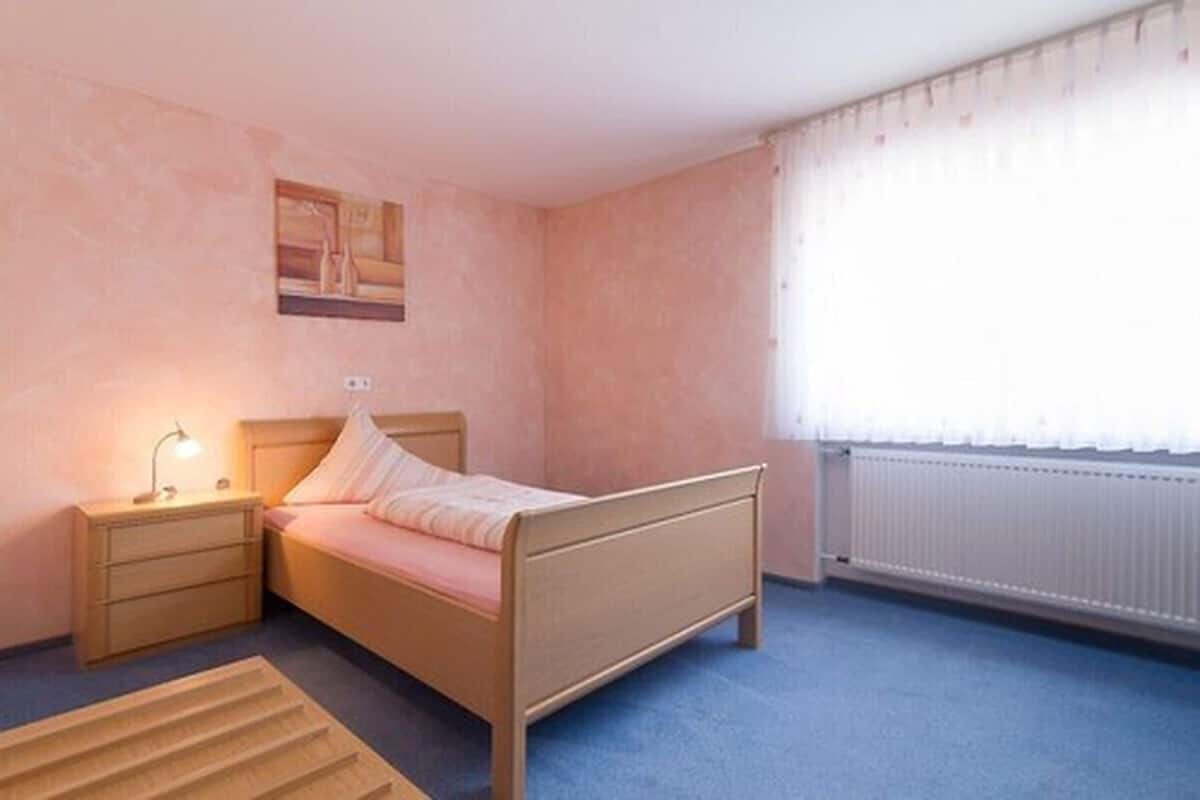 Un dormitorio con cama, mesita de noche, lámpara y ventana con cortinas.
