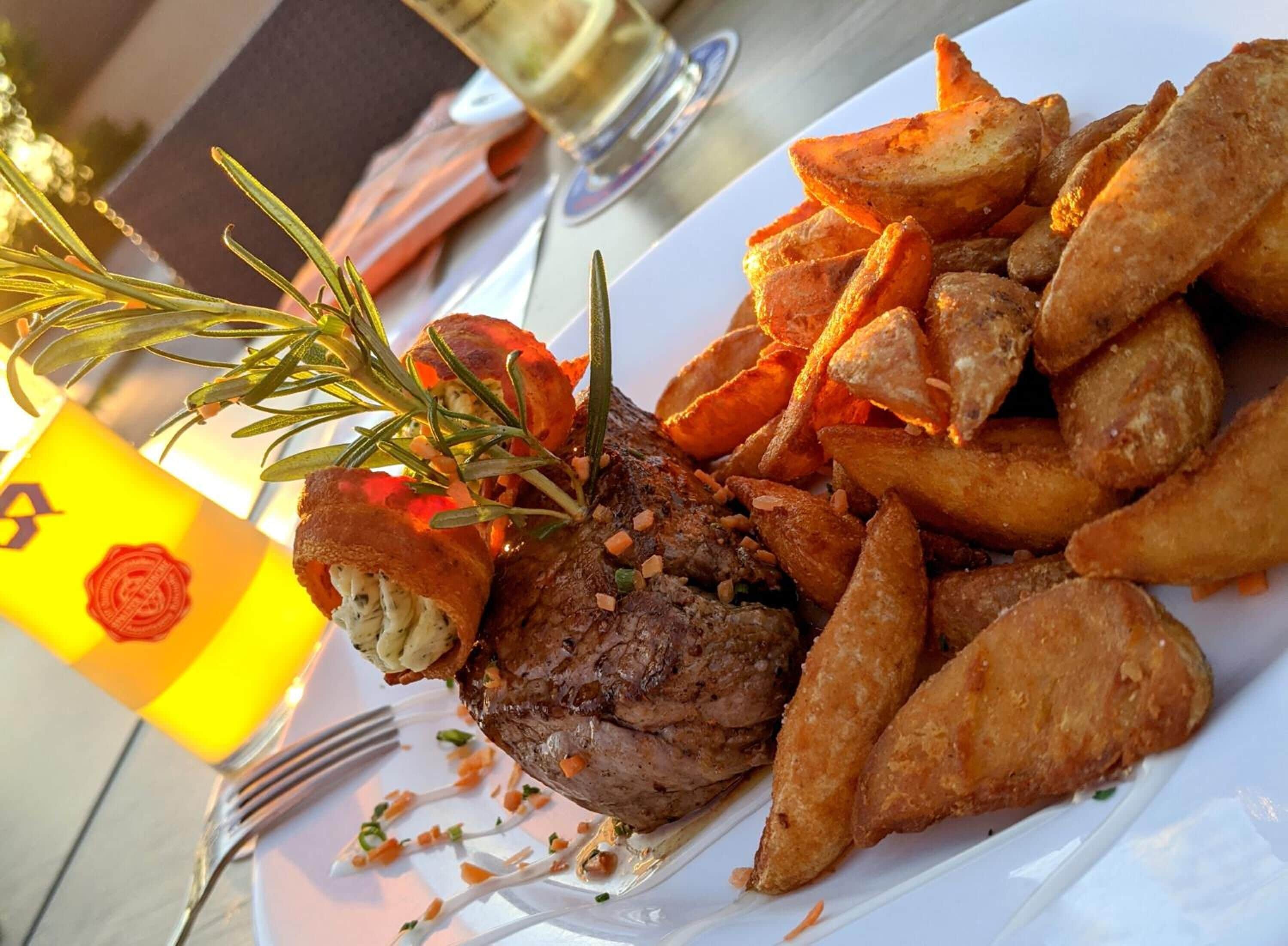 Een bord eten met een steak, friet en een rozemarijn garnituur.