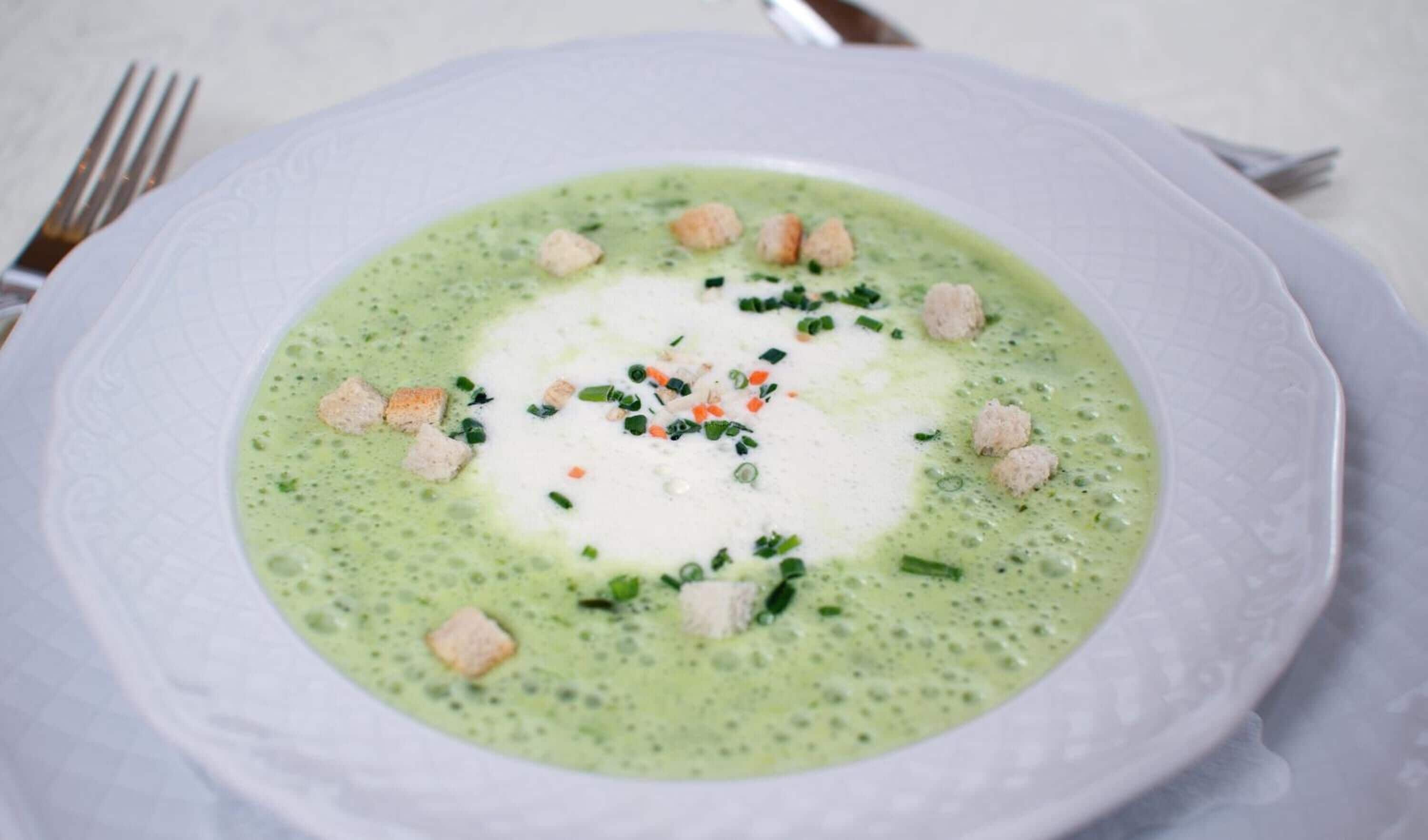 A bowl of green soup garnished with croutons and herbs.