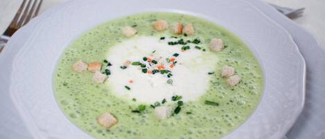 A bowl of green soup garnished with croutons and herbs.
