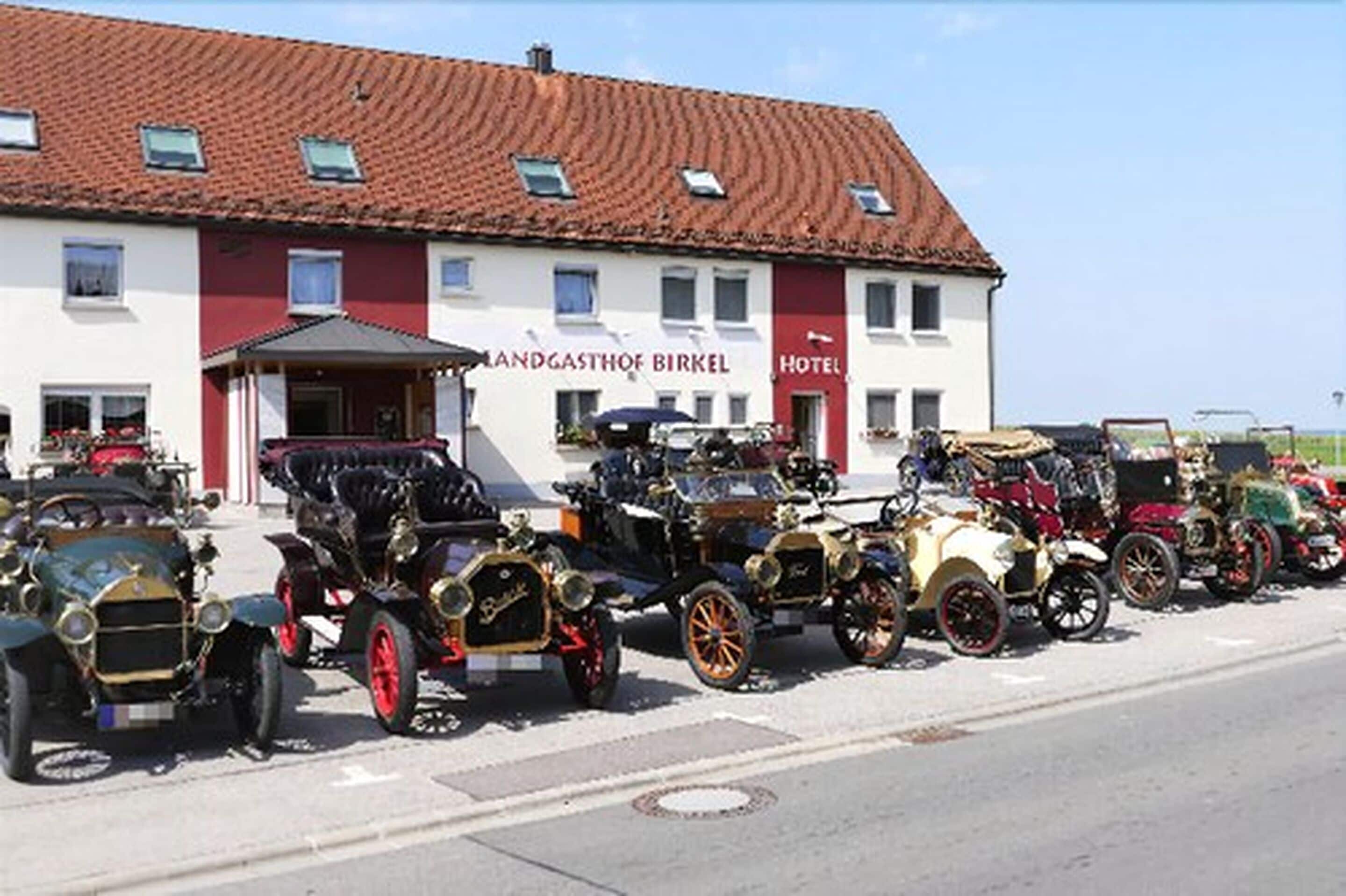 Une rangée de voitures anciennes est garée devant un bâtiment portant l’inscription « Landgasthof Birkel Hotel ».