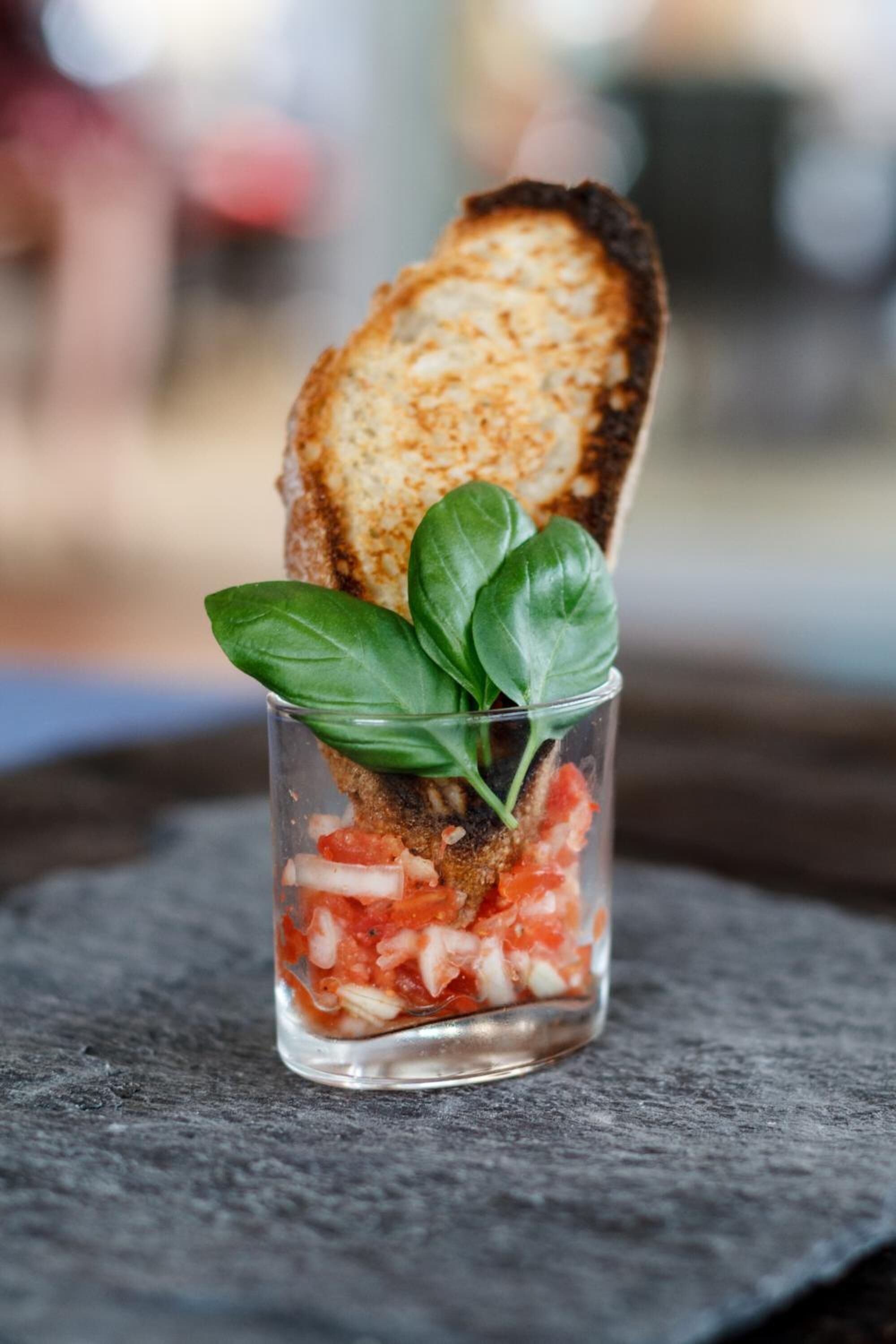 A toasted bread slice with a basil leaf on top, placed on a dark surface.