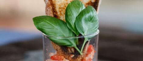 Una rebanada de pan tostado con una hoja de albahaca encima, sobre una superficie oscura.