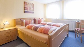 Una cama doble con ropa de cama a rayas, una mesita de noche con lámpara y una silla.