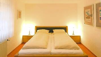 Una cama doble con estructura de madera, dos mesitas de noche con lámparas y cuadros enmarcados en las paredes.
