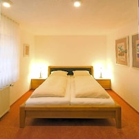 Una cama doble con estructura de madera, dos mesitas de noche con lámparas y cuadros enmarcados en las paredes.