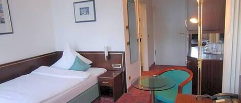 A hotel room with a bed, bedside table, chair, desk, and a telephone.