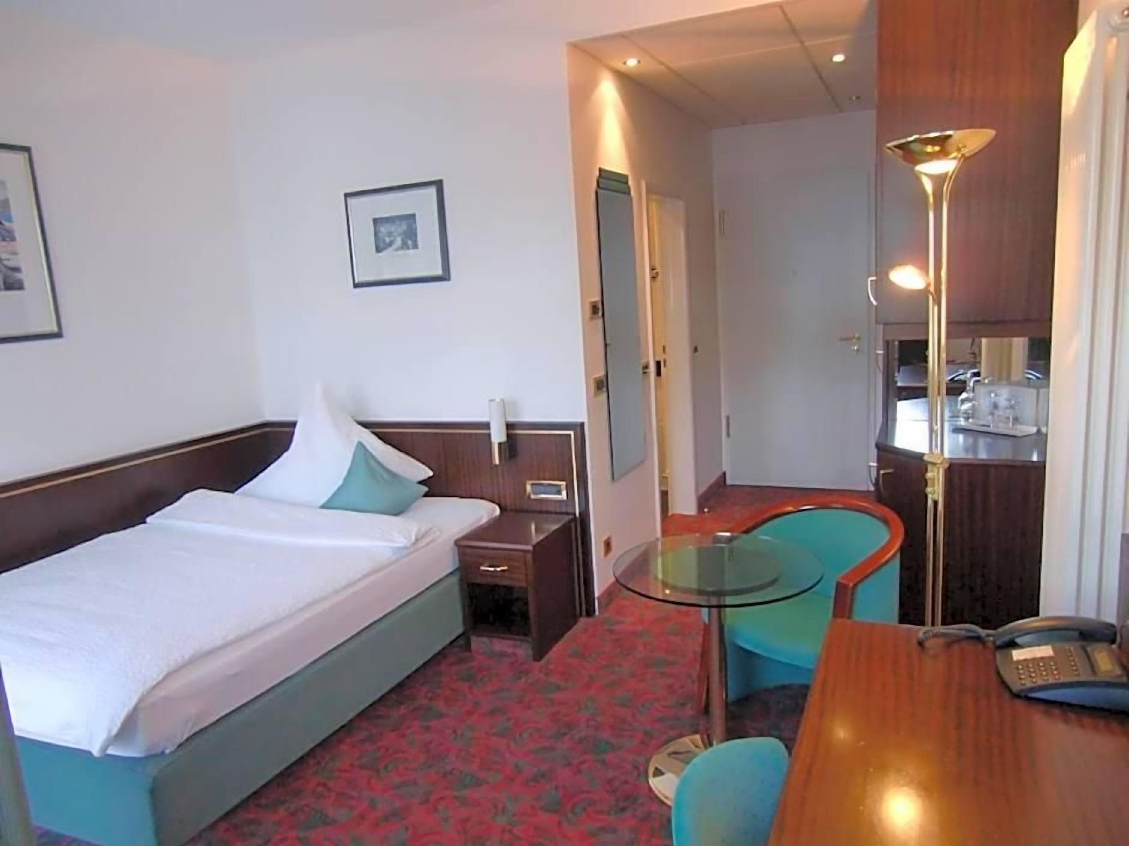 A hotel room with a bed, bedside table, chair, desk, and a telephone.