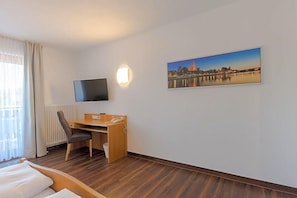A hotel room with a bed, a desk, a chair, a television, a picture on the wall, and a window with curtains.