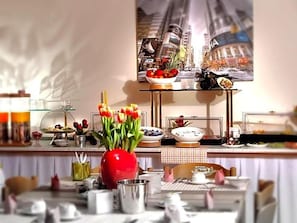 A breakfast buffet with a variety of food items, a vase of tulips, and a cityscape poster on the wall. - Bartholomäus (Zeitlarn)