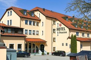 A multi-story hotel with a red-tiled roof and a sign indicating it is a pension.