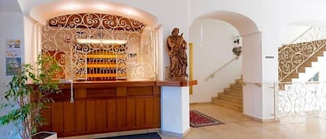A reception area with a wooden counter, a statue, and a staircase with a wrought iron railing.