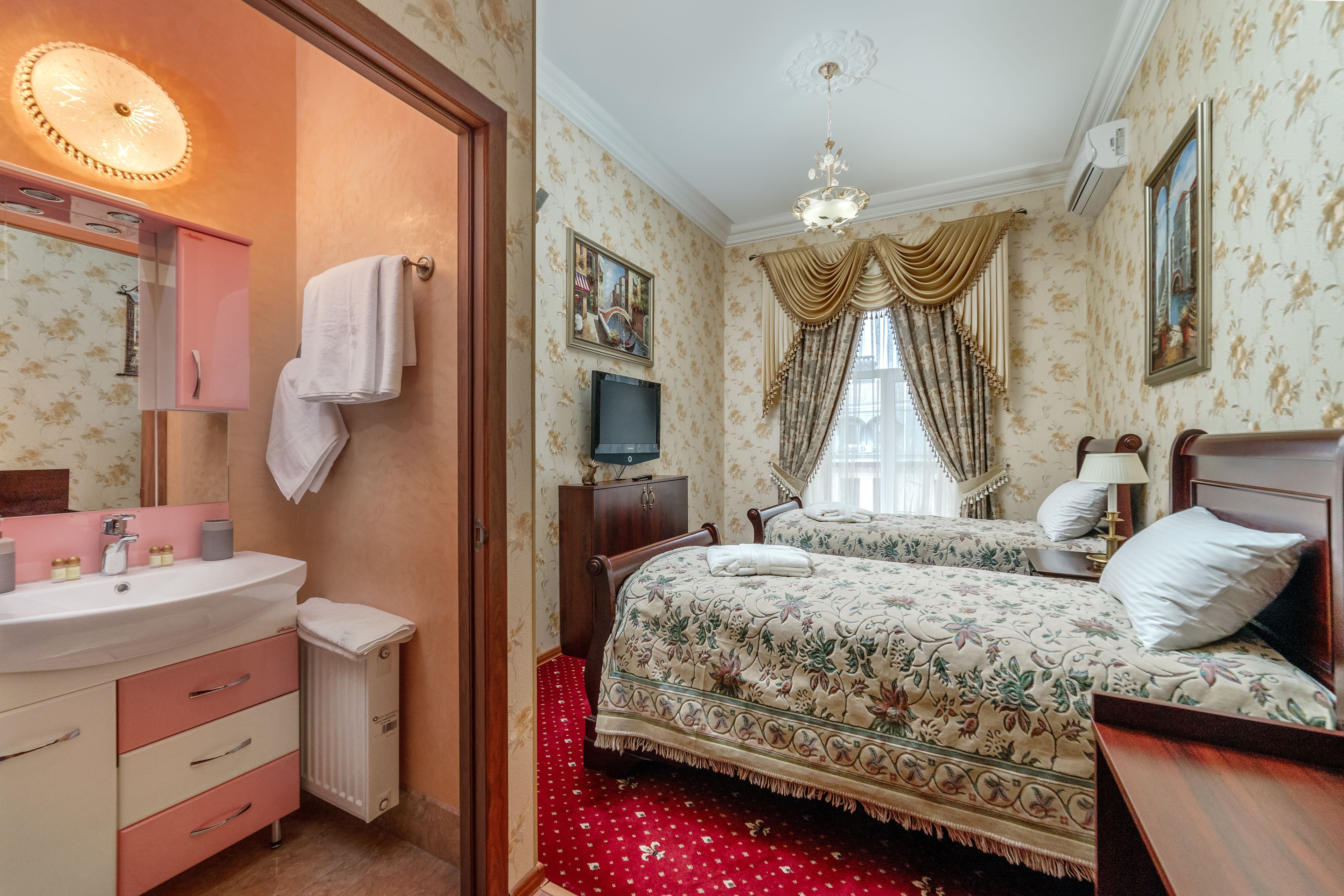 Une chambre d’hôtel avec salle de bain, un lit avec une literie à motifs floraux, une télévision et un lustre.