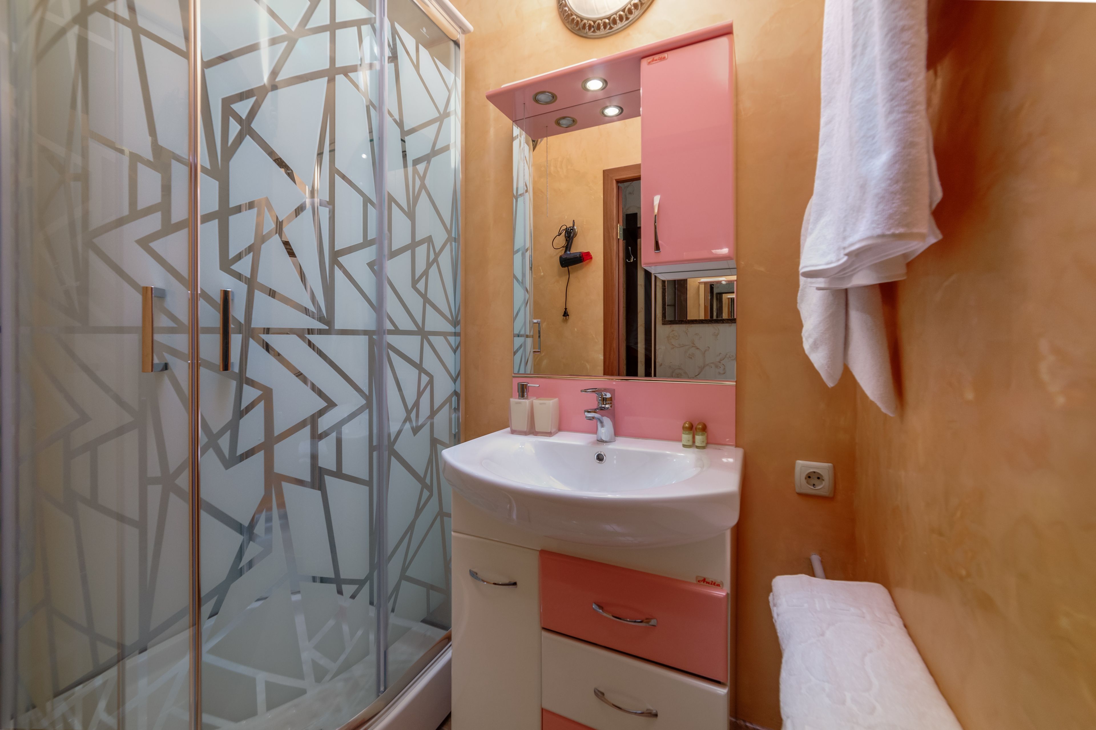 Ein Badezimmer mit einer Duschkabine aus Glas, einem rosa Waschtisch mit Spiegel und einem weißen Handtuch an der Wand.