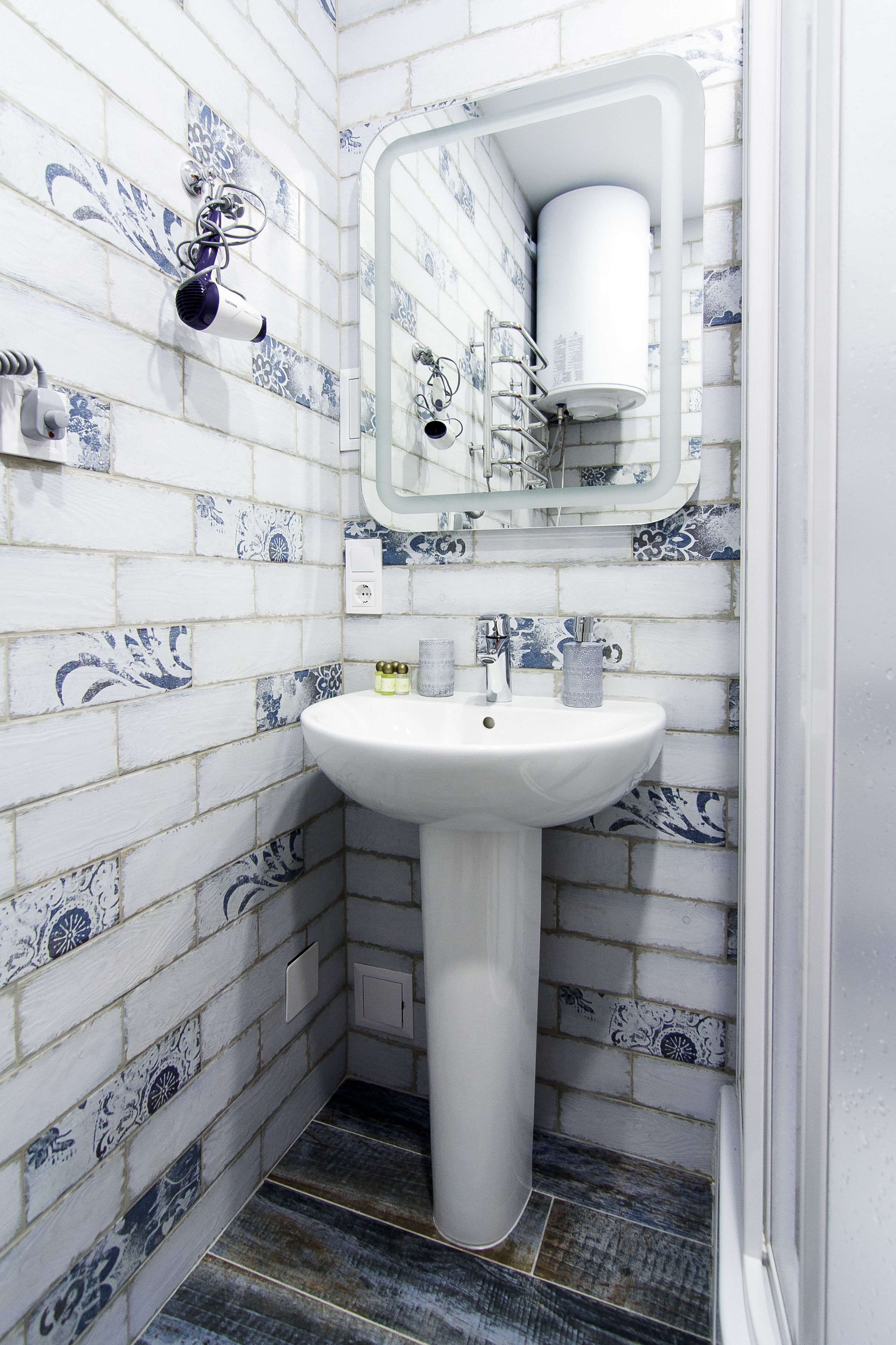 Un baño con un lavamanos pedestal blanco, un espejo y azulejos blancos y azules con diseño.