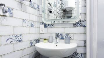 Un baño con un lavamanos pedestal blanco, un espejo y azulejos blancos y azules con diseño.