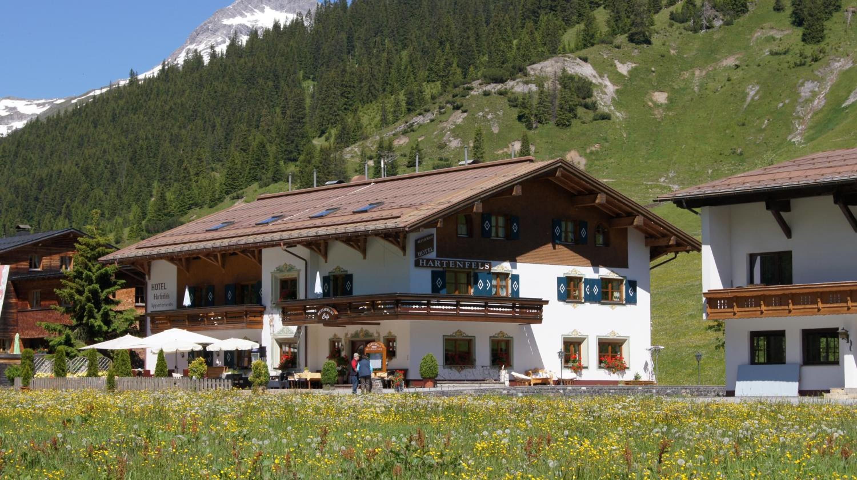 A hotel with a traditional Alpine architectural style, featuring a prominent balcony and a mountain backdrop.