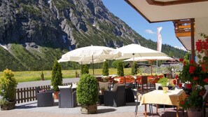 An outdoor seating area with tables and chairs, umbrellas, and potted plants.