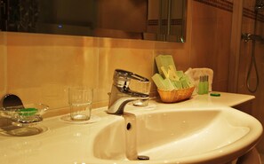 A bathroom sink with a chrome faucet, a glass of water, a soap dispenser, and a basket of toiletries.