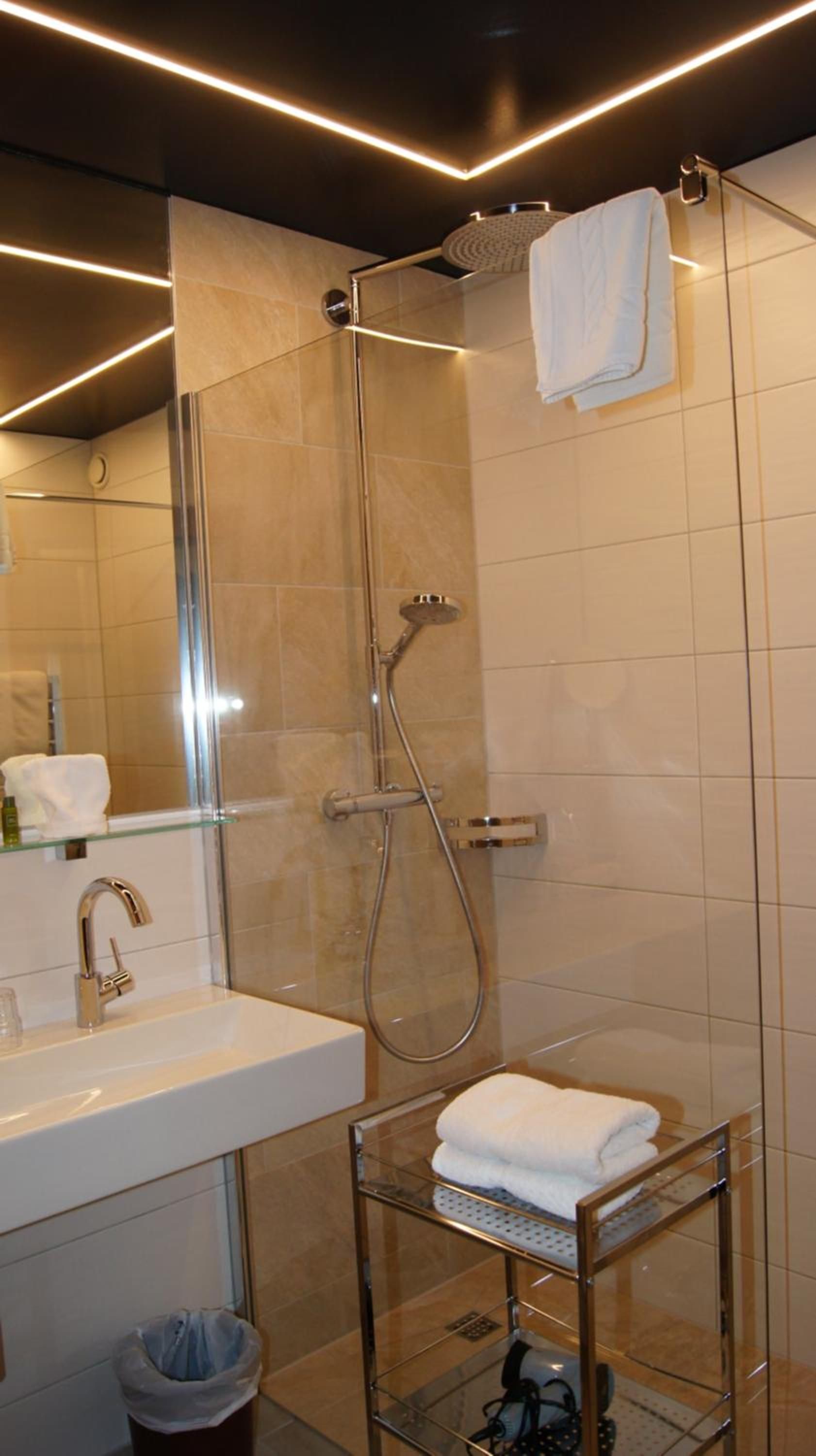 Casa de banho moderna com cabine de chuveiro em vidro, lavatório branco e prateleira de vidro com uma toalha.