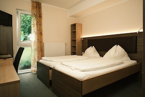 A double bed with a wooden headboard, a bedside table, a desk, and a chair.