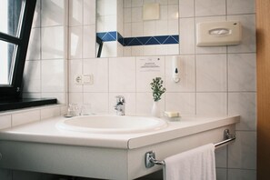 Une salle de bain moderne avec un lavabo blanc, un miroir, un porte-serviettes et un distributeur de savon.