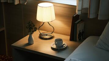 Ein ordentlich bezogenes Bett mit einem weißen Kopfkissen, ein Nachttisch mit einer Lampe, einer Tasse und einer kleinen Pflanze.