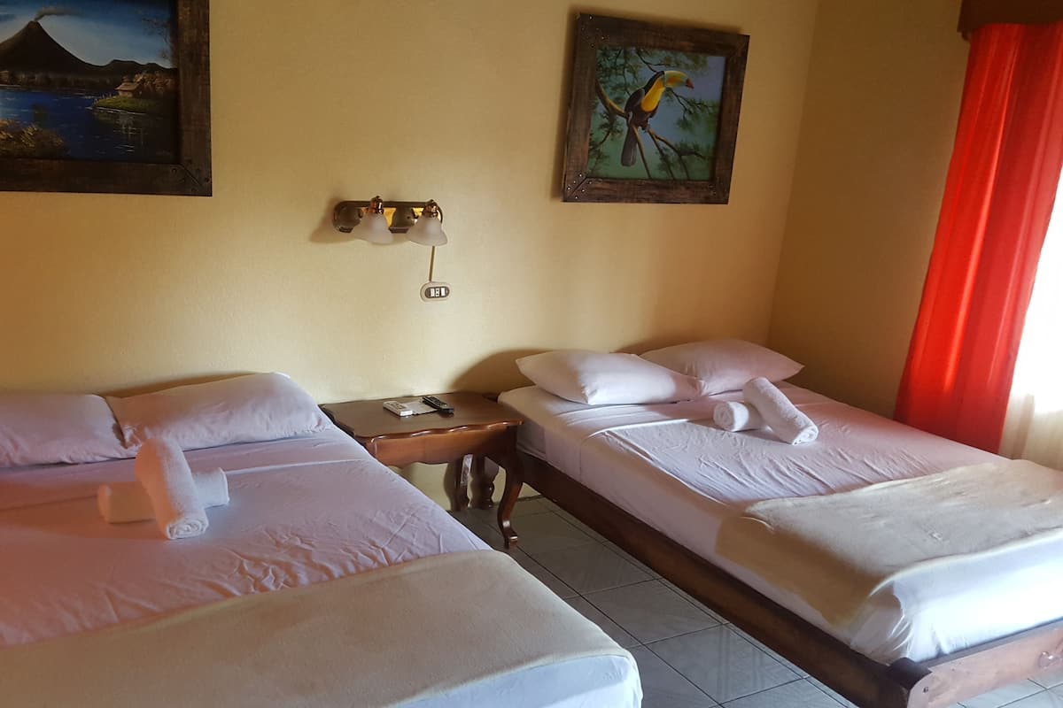 Ein Hotelzimmer mit zwei Betten, einem Nachttisch, einem Vulkanszenen-Gemälde, einem Vogel-Gemälde und einem roten Vorhang.