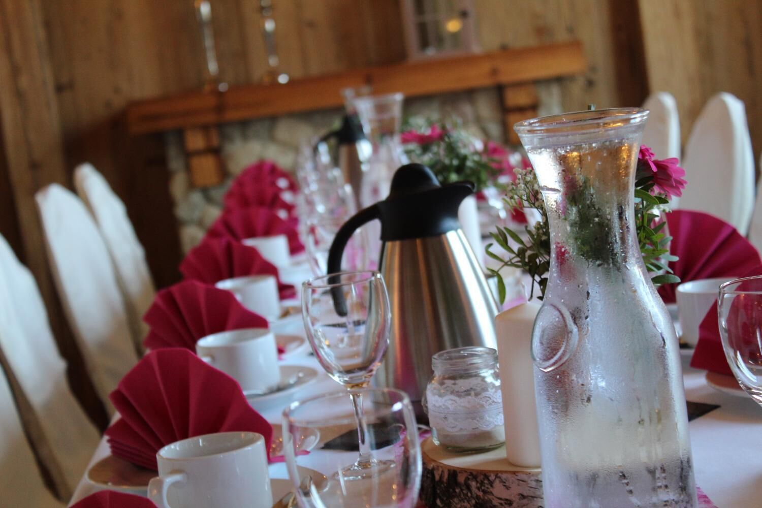 Een gedekte tafel met witte tafellinnen, roze servetten en glazen.