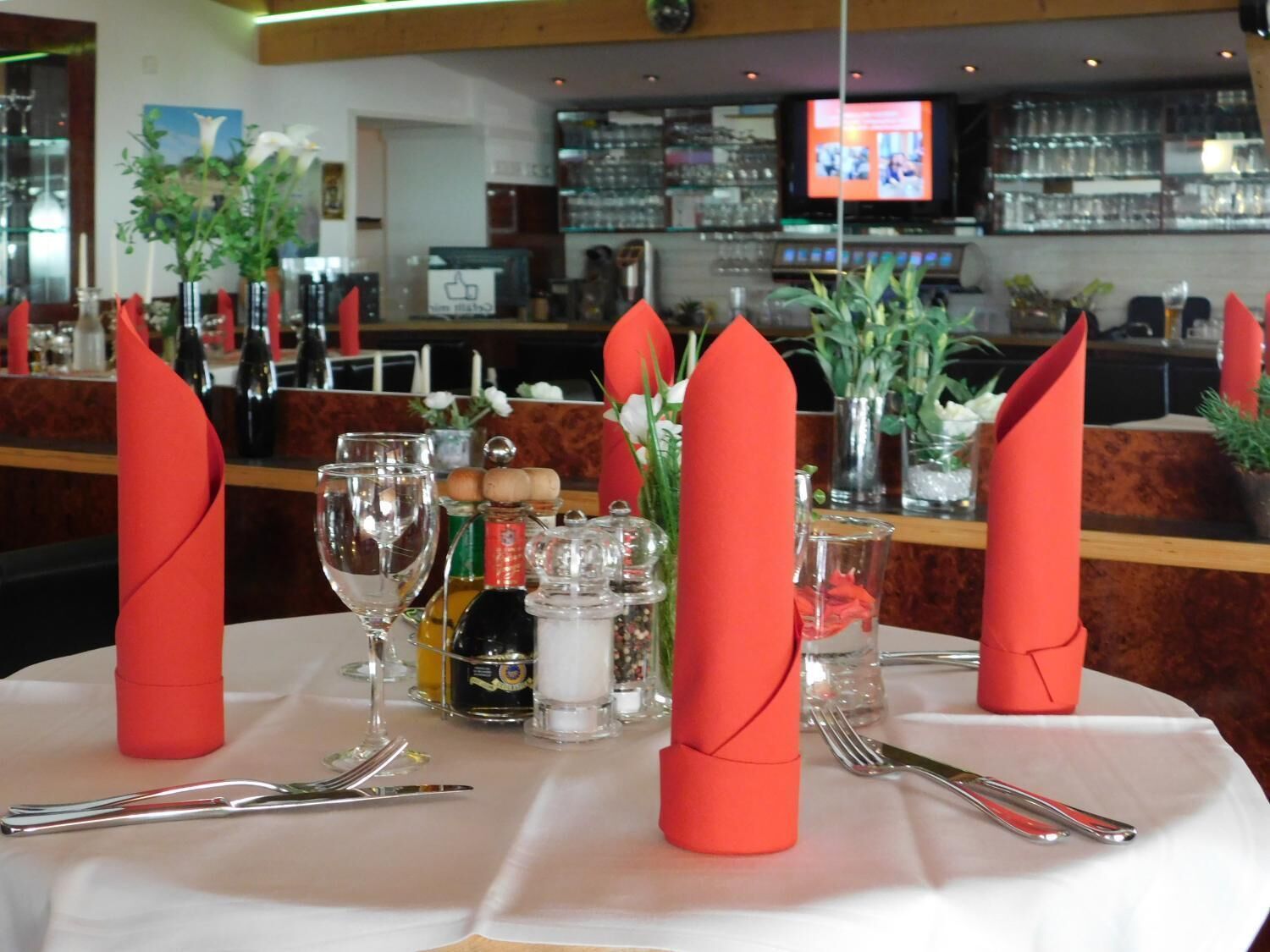 Une table de restaurant dressée avec des serviettes rouges, des verres à vin et des couverts.